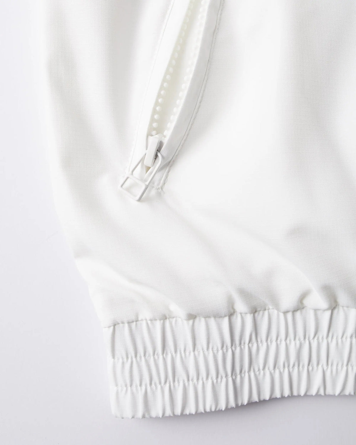 Detail of the white byParra Tennis Maybe? Track Jacket featuring a zippered pocket and elasticated hem.