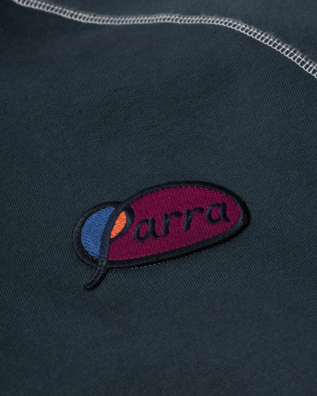 Embroidered Parra script logo patch detail on a dark blue hooded sweatshirt.