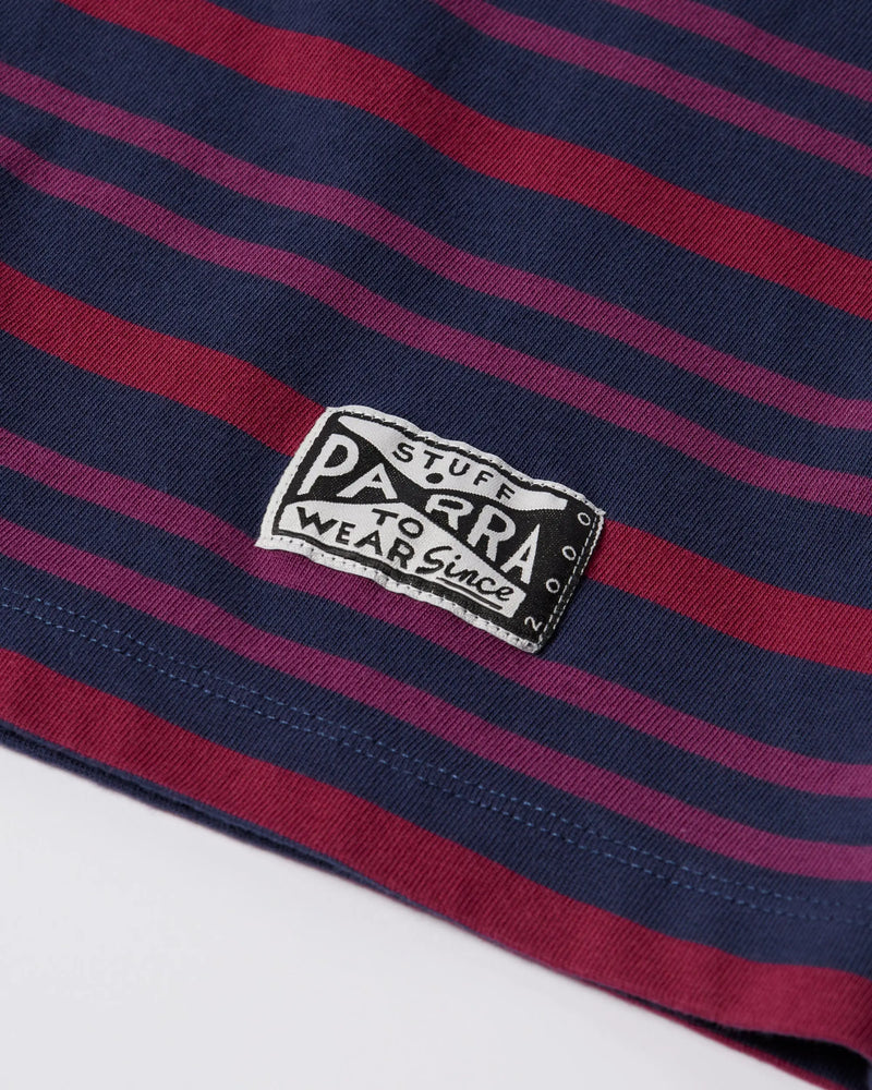Close-up of the woven logo patch on a purple striped byParra 1992 long sleeve t-shirt.