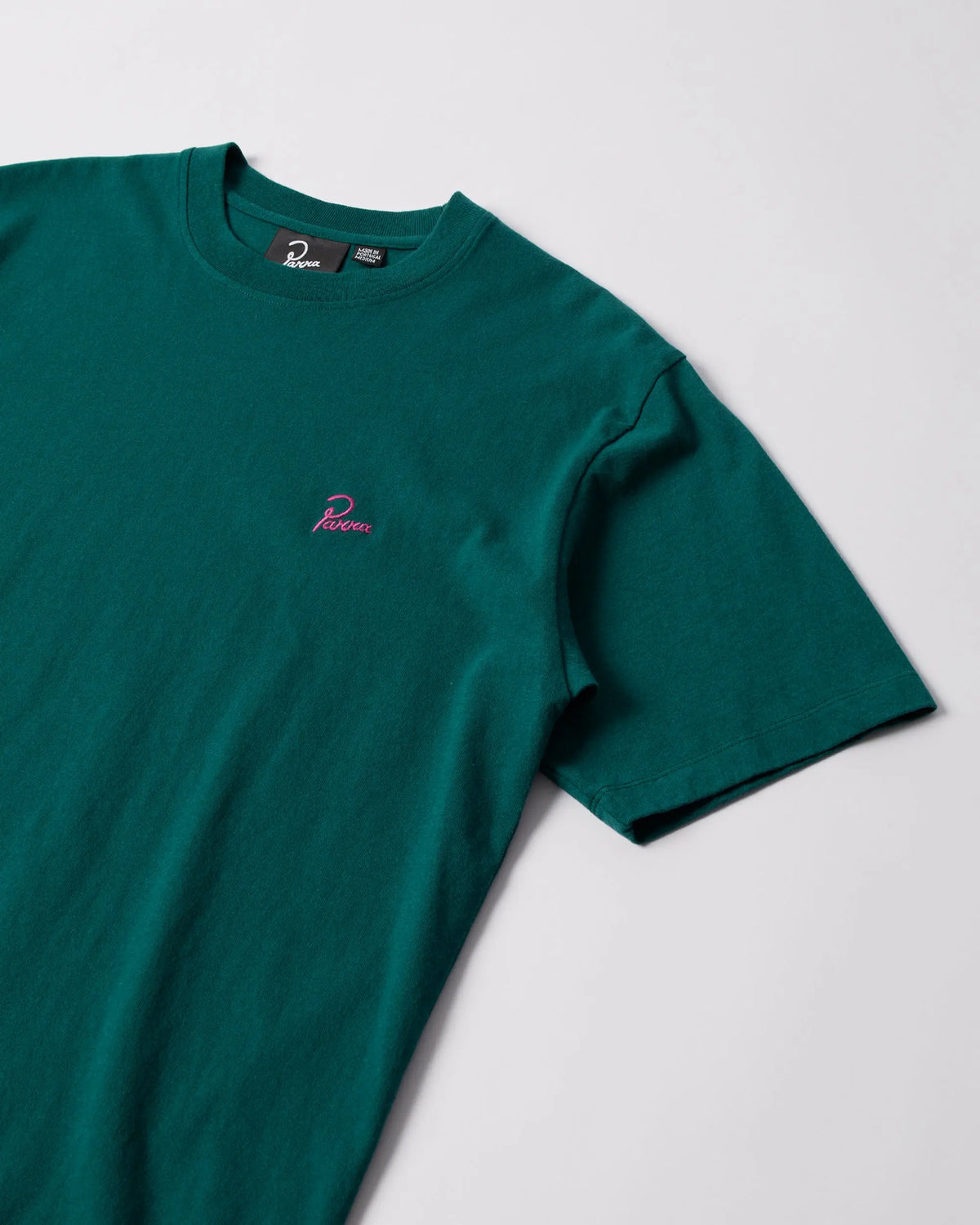 Close-up of the dark green byParra Signature cotton t-shirt with pink embroidered chest logo.