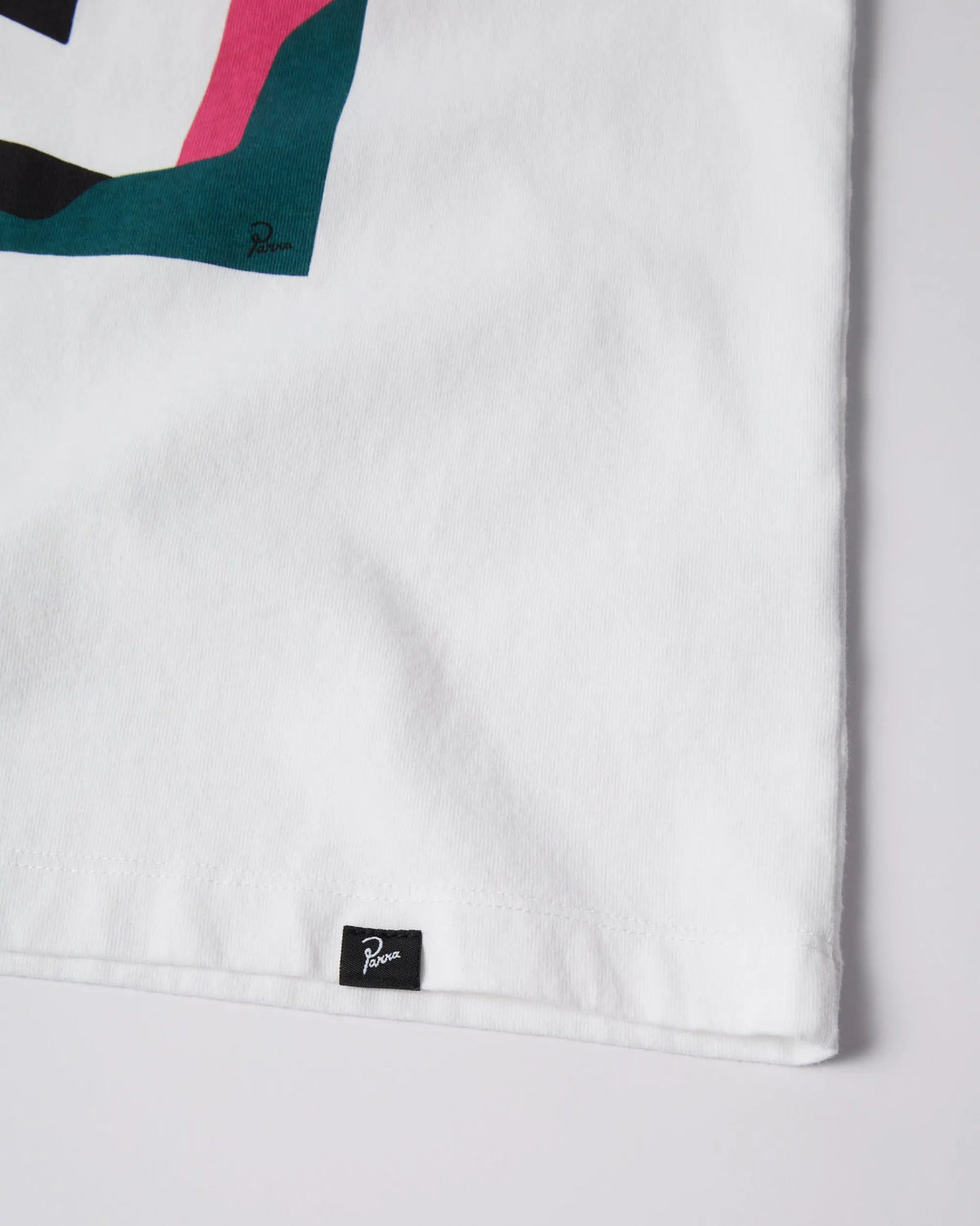 Close-up of the woven logo tag on the hem of the white By Parra No Vacation t-shirt.