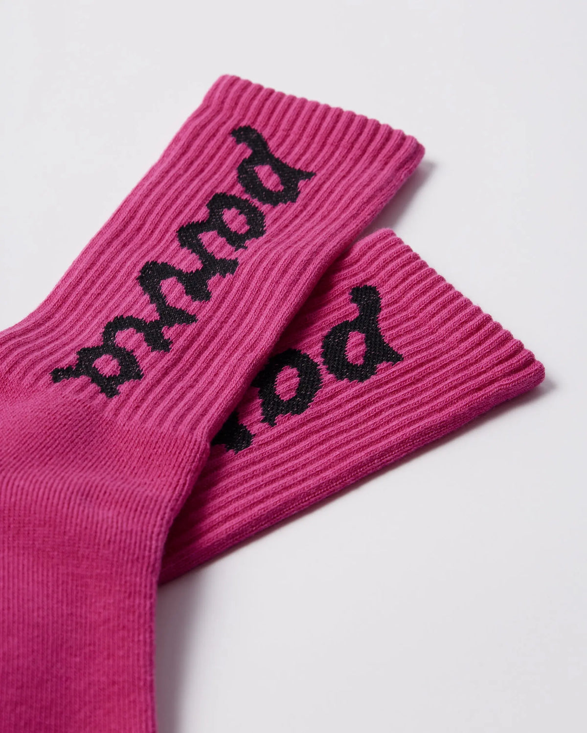 Close-up of By Parra hot pink ribbed crew socks featuring black lowercase script logo branding.