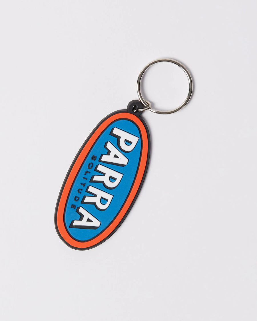 By Parra Lonely oval rubber keychain in blue and orange with logo graphics.