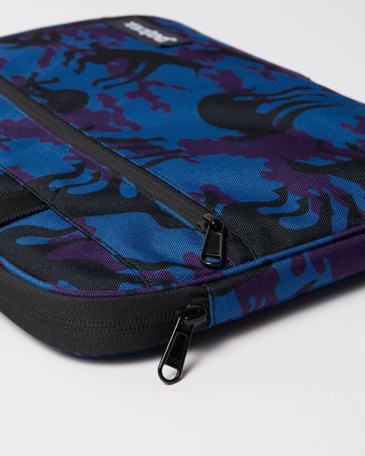 Detail view of the By Parra Purple Camo Beast laptop sleeve showing black zippers and patterned fabric.