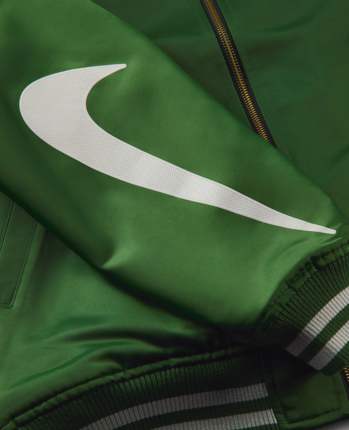 Close-up of the white Swoosh logo on the forest green sleeve of the Nike x NIGO NRG Coach Jacket.