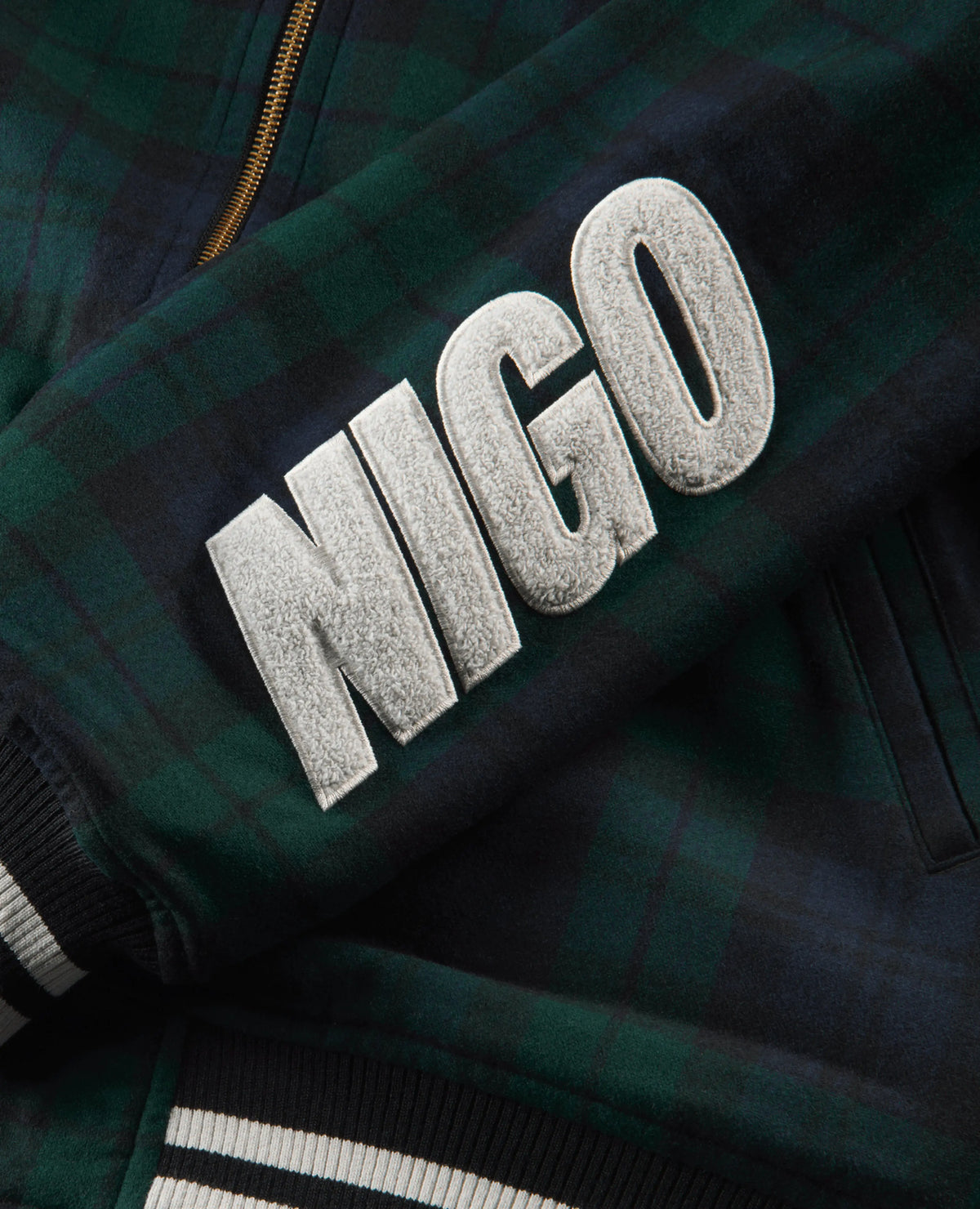 Close-up of white chenille NIGO lettering on the green plaid Nike x NIGO coach jacket.