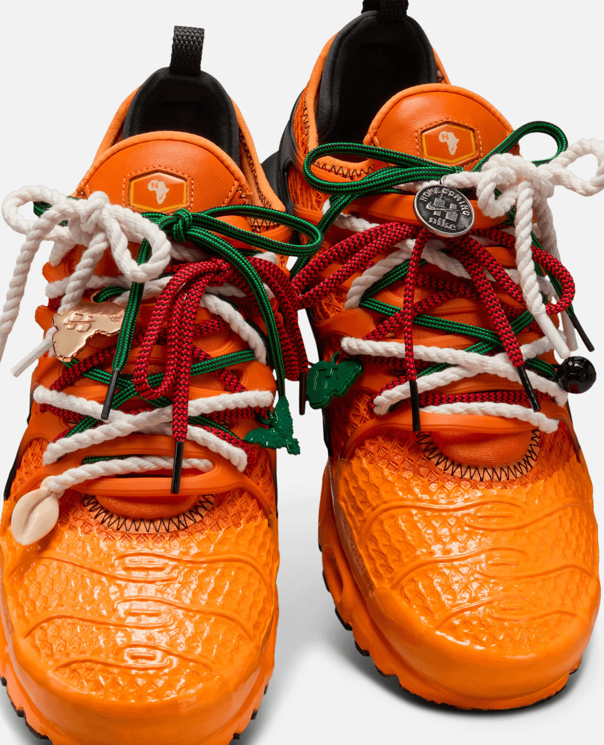 Close-up of Safety Orange HOMECOMING x Nike Air Max Plus sneakers with colorful layered laces and lace charms.