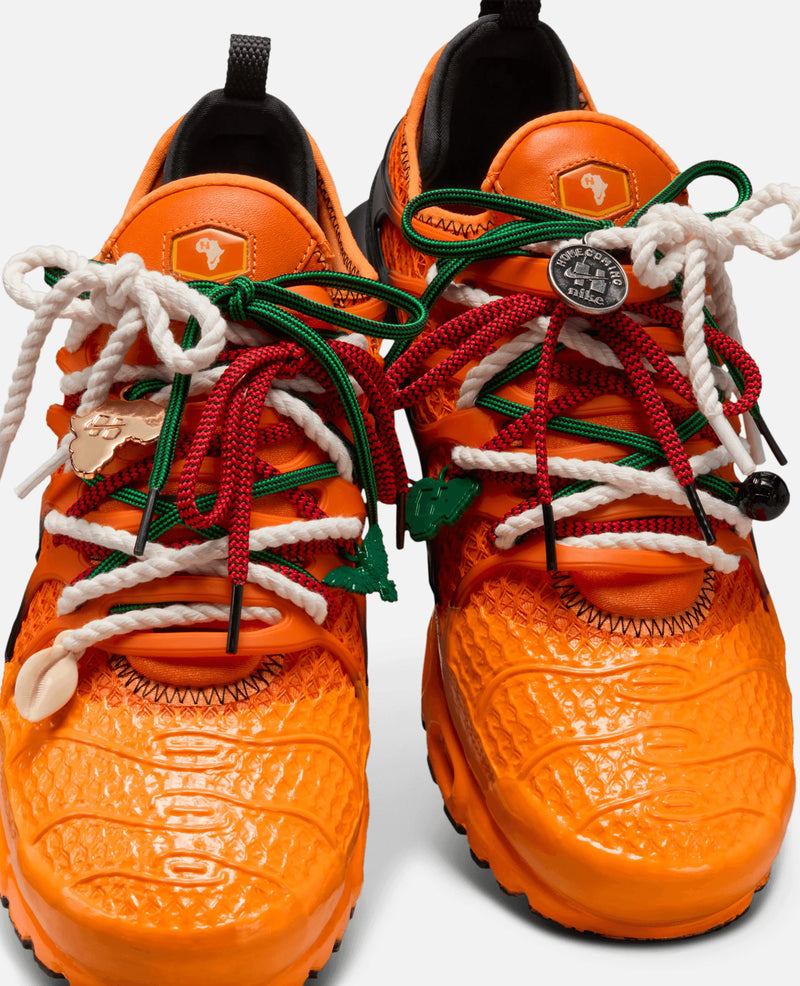 Close-up of Safety Orange HOMECOMING x Nike Air Max Plus sneakers with colorful layered laces and lace charms.