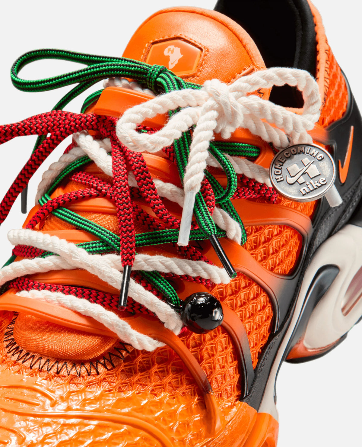 Close-up of HOMECOMING x Nike Air Max Plus in safety orange with layered rope laces and a metallic lace charm.