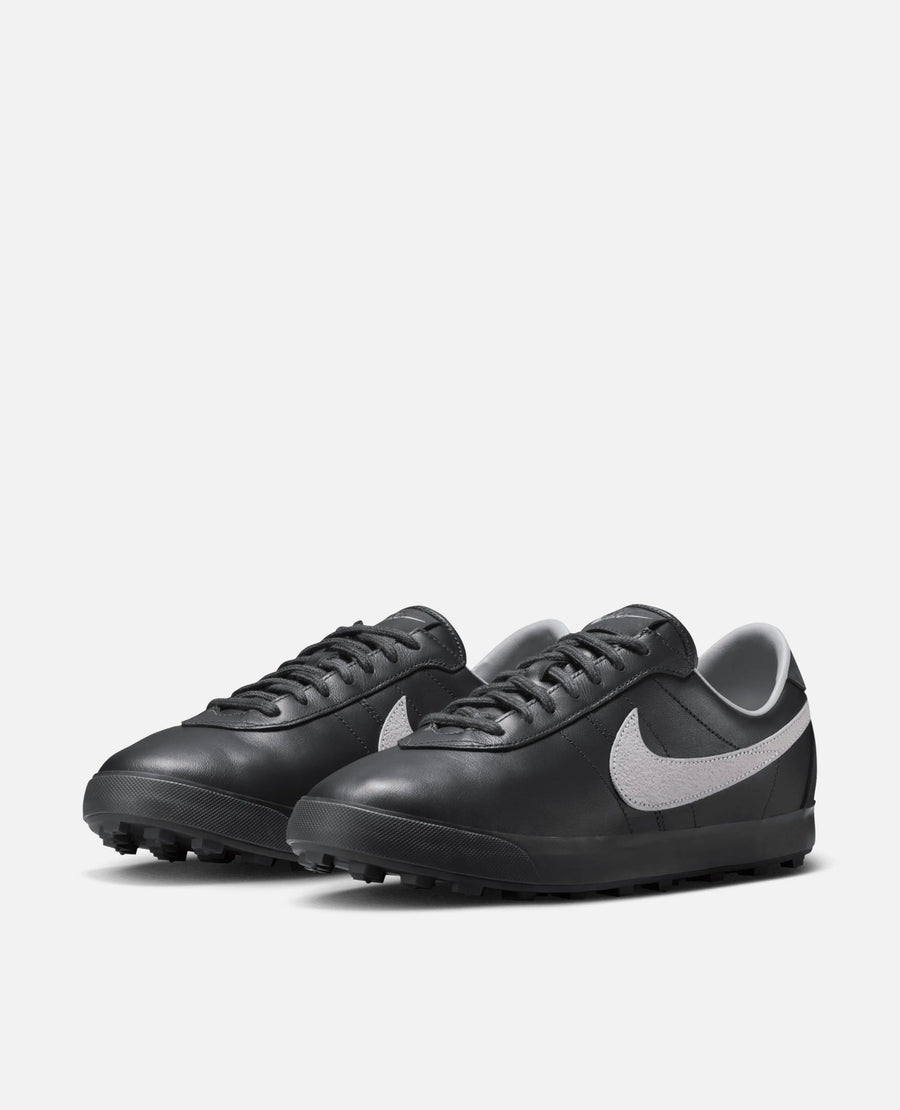 Nike Astrograbber sneakers in Off Noir black leather with Cement Grey Swooshes in a three-quarter view.