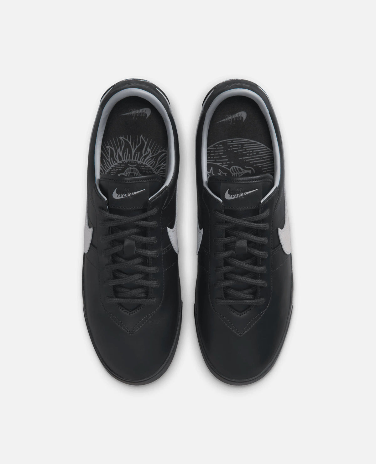 Top-down view of black leather Nike Astrograbber sneakers with cement grey accents and graphic insoles.