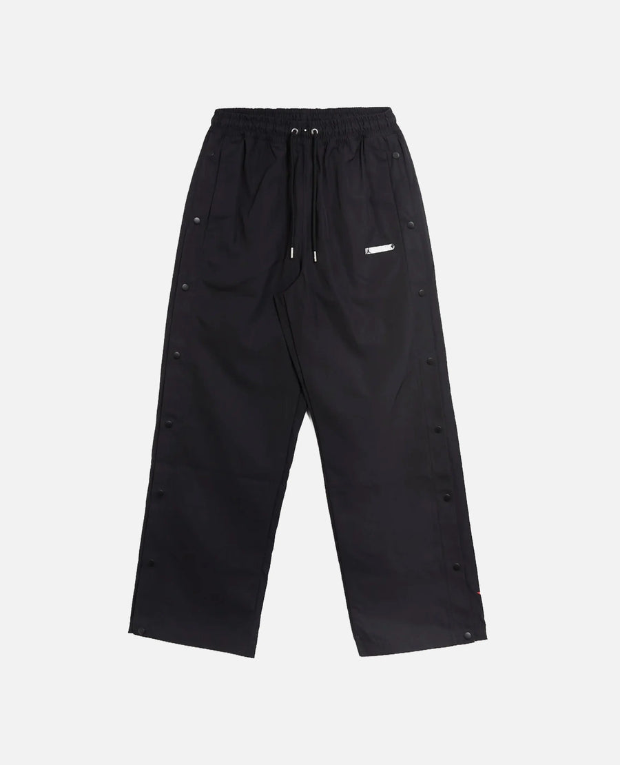 Front view of Nike Jordan x FTY men's black track pants featuring side snap buttons.