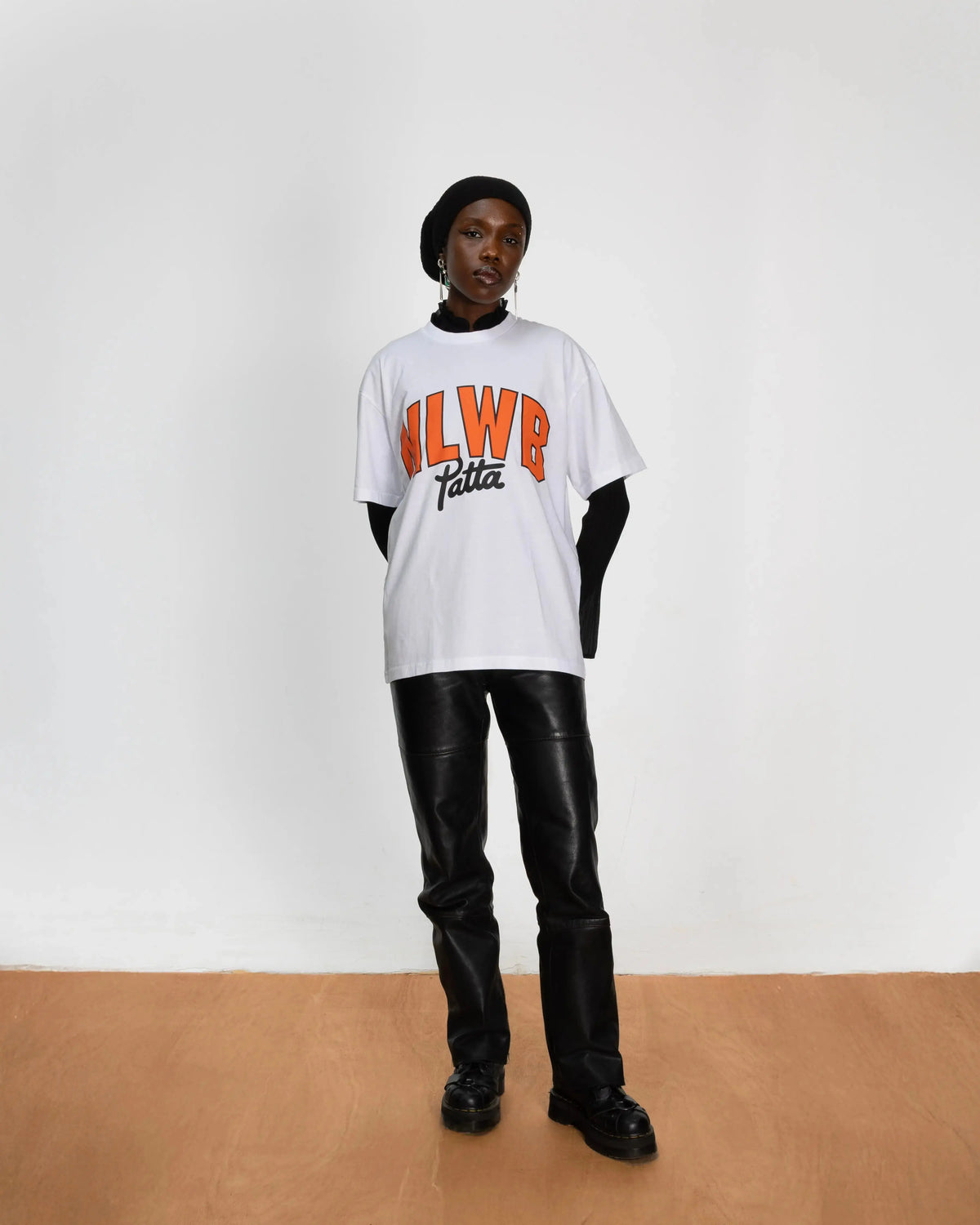 Model wearing the white Patta x NLWB 15th Anniversary T-shirt styled with black leather pants.