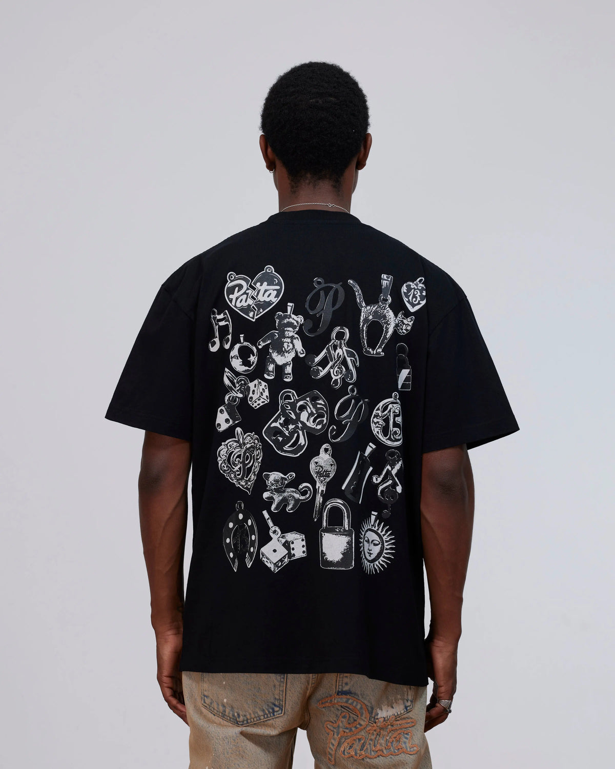 Back view of model wearing the black Patta Charm T-Shirt with white charms graphic print.
