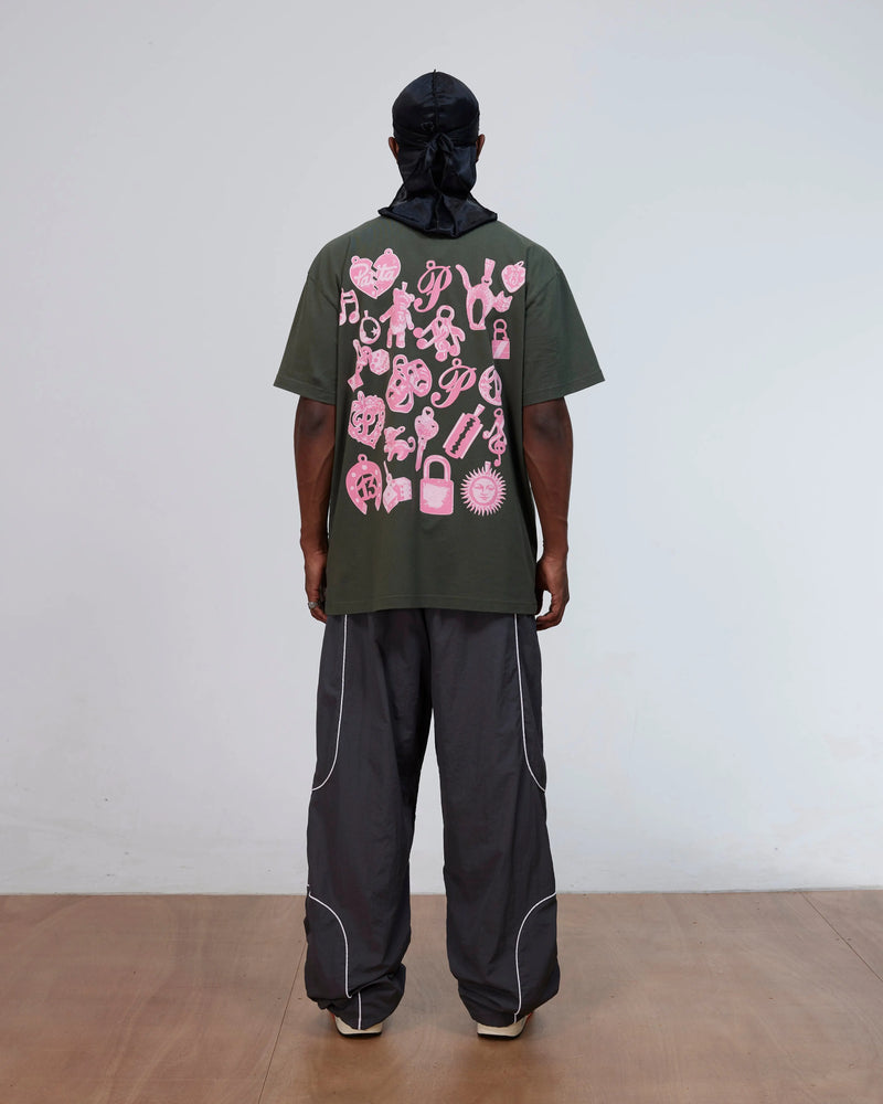 Back view of model wearing the Patta Charm T-Shirt in Climbing Ivy green with pink graphics on the back.