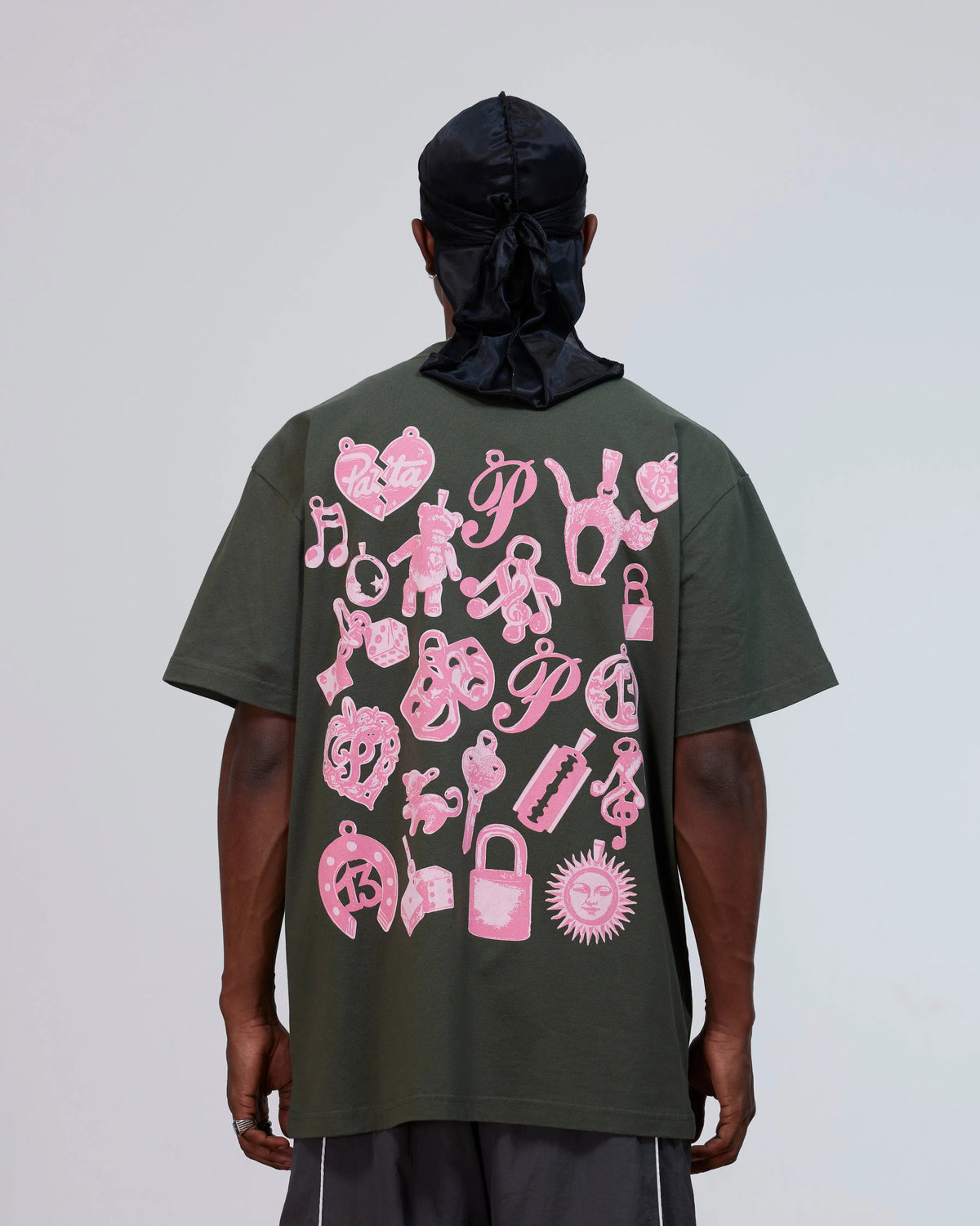 Back view of a model wearing the Patta Charm T-Shirt in climbing ivy green with pink charms artwork.