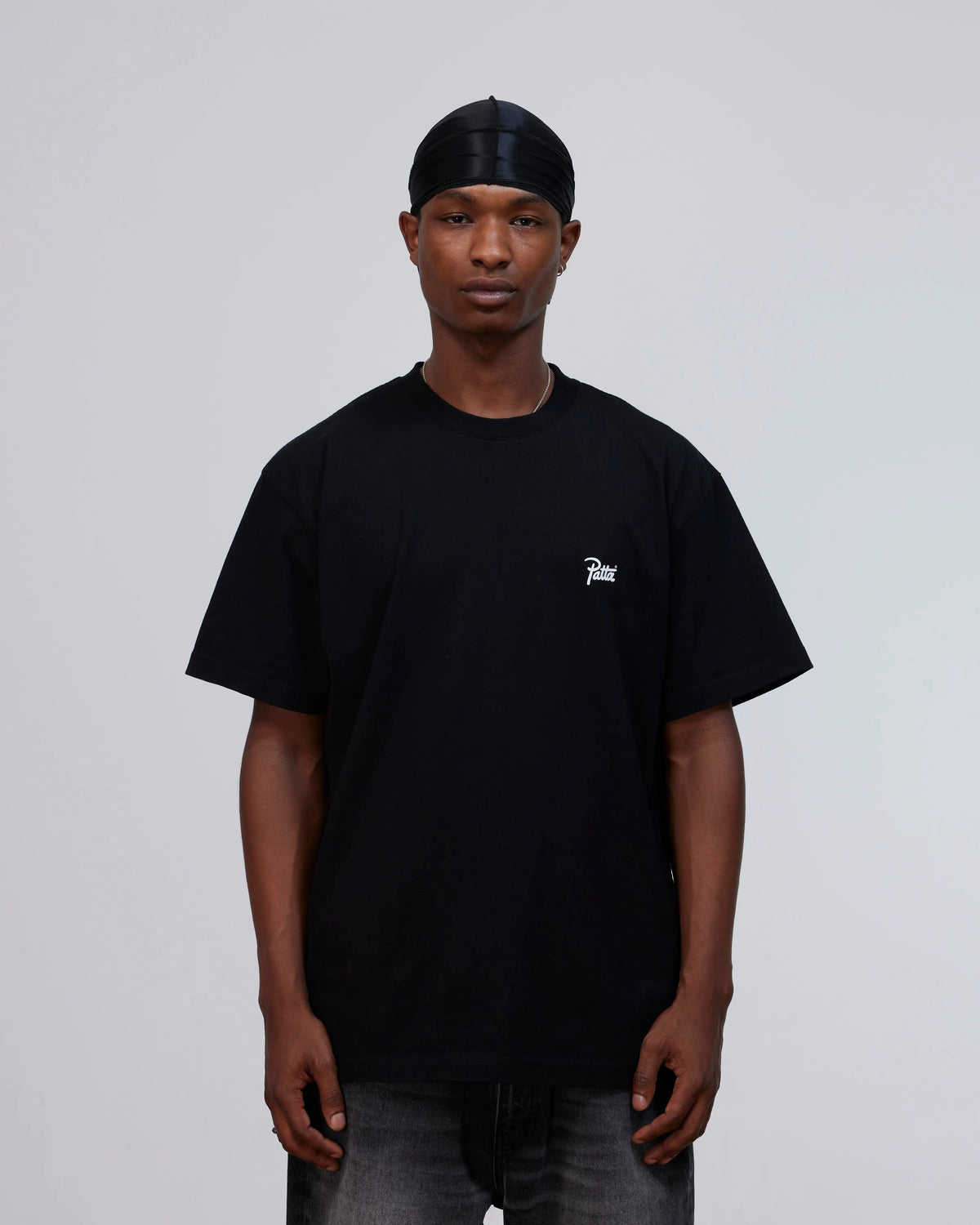 Model wearing the black Patta Championship cotton T-shirt with a white script logo on the chest.