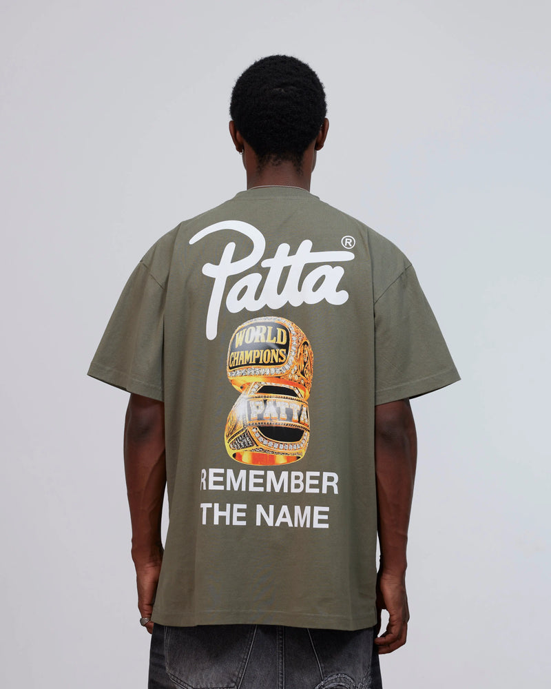 Back view of model wearing the Patta Championship T-Shirt in dusty olive with graphic print.