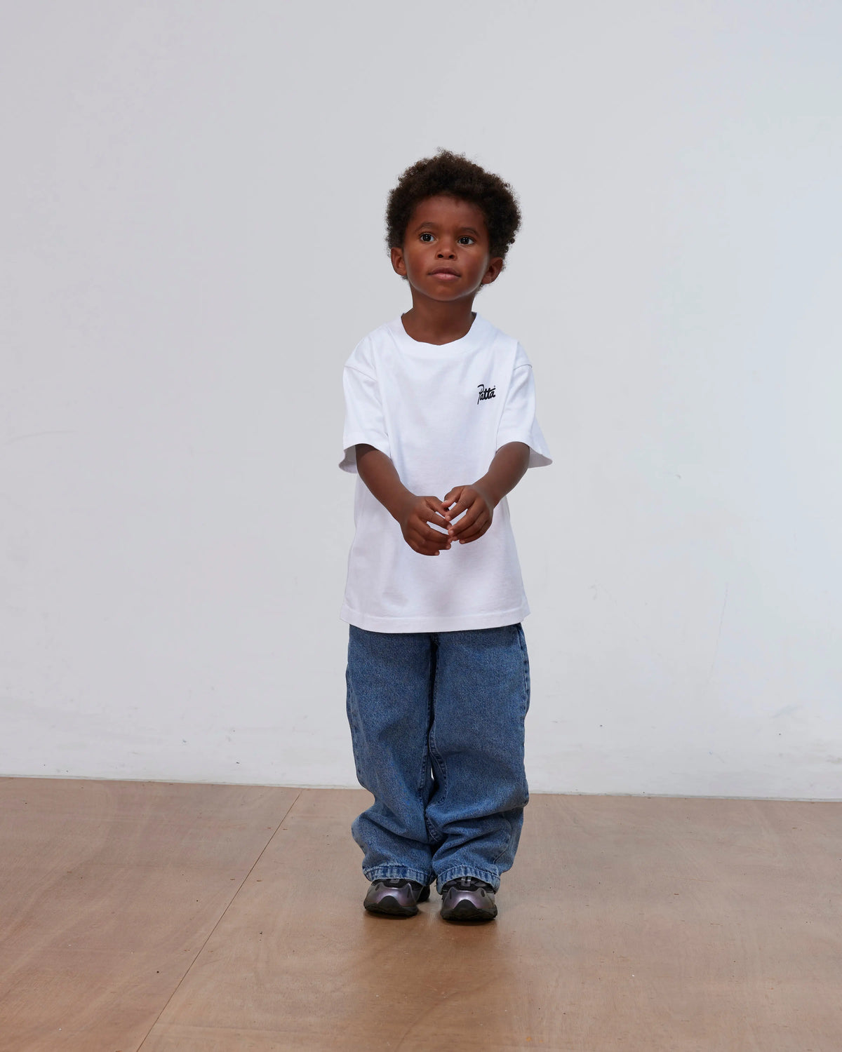 Front view of a child wearing the white Patta Kids Charm T-Shirt with blue denim jeans.