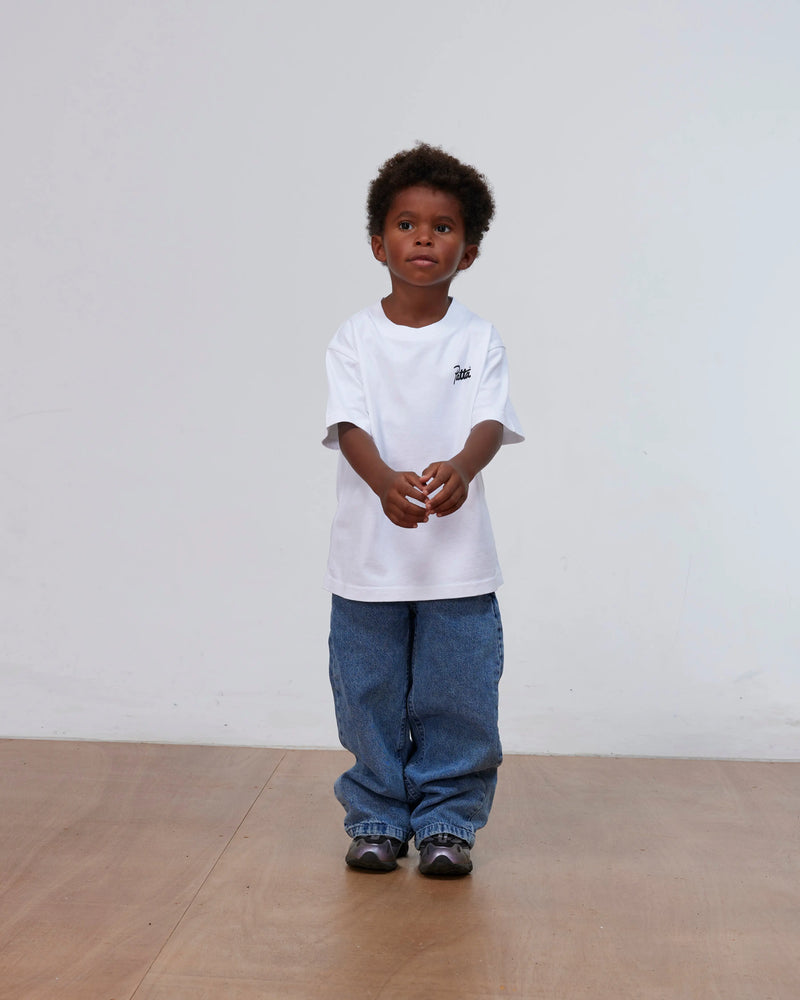 Front view of a child wearing the white Patta Kids Charm T-Shirt with blue denim jeans.