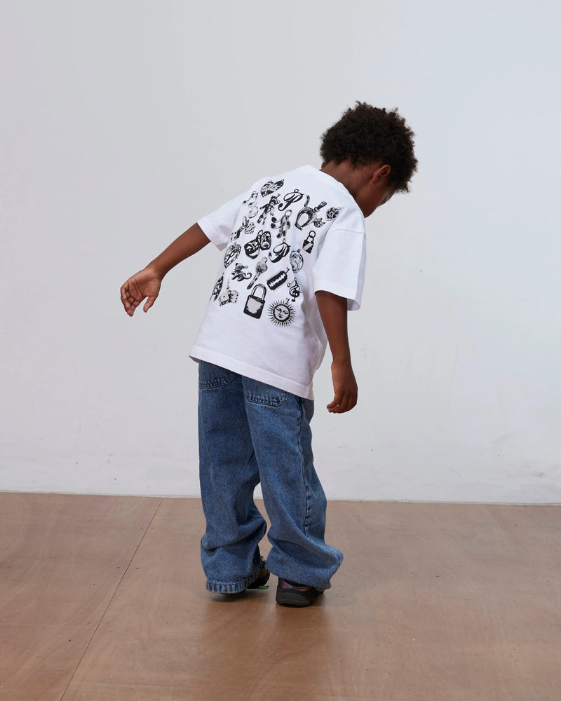 Child wearing the white Patta Kids Charm T-Shirt with back charm graphics and loose denim jeans.