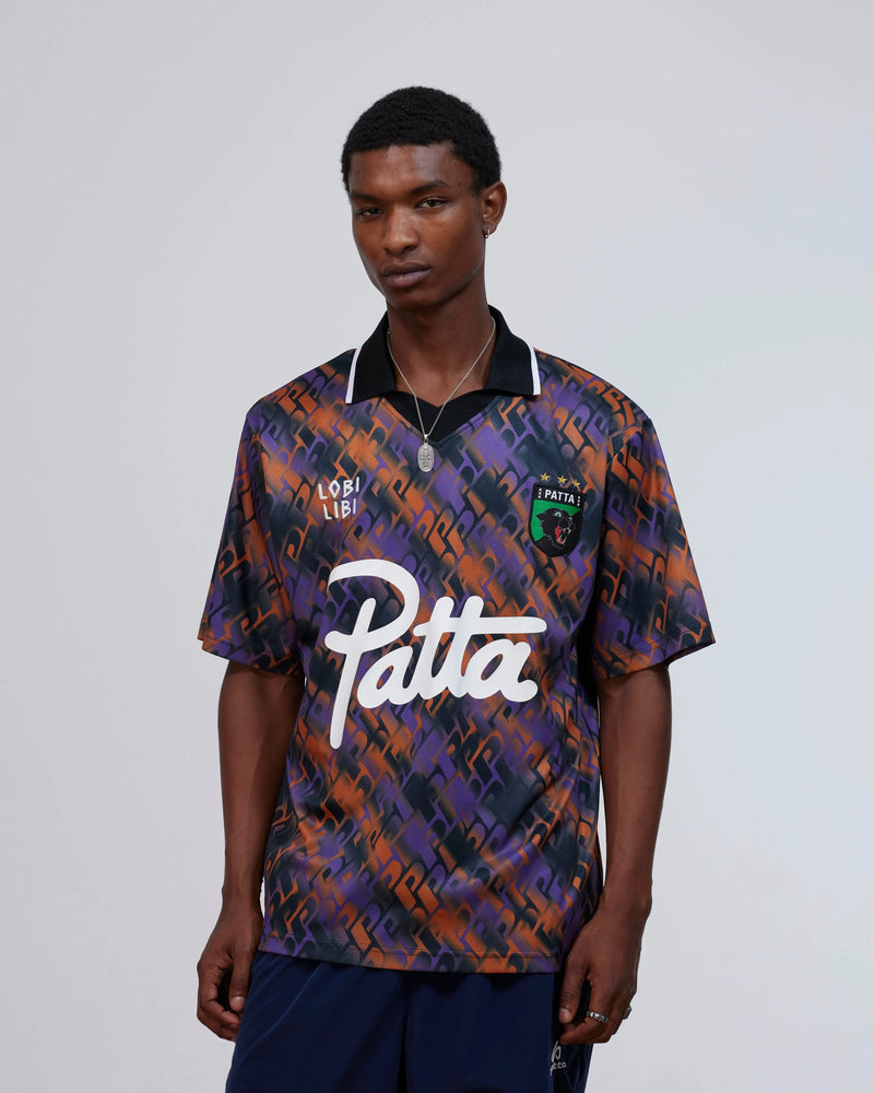 Model wearing the Patta All Over P Football Jersey in pansy purple and orange with script logo.