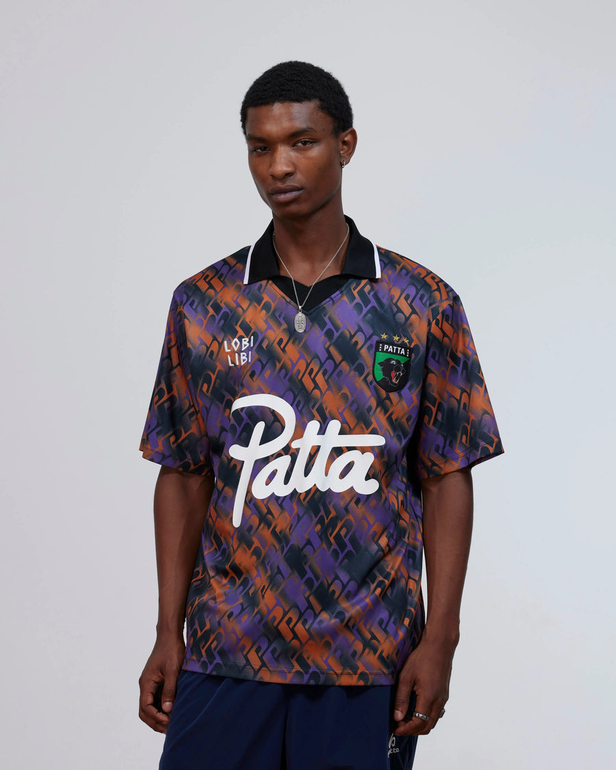 Model wearing the Patta All Over P Football Jersey in pansy purple and orange with script logo.