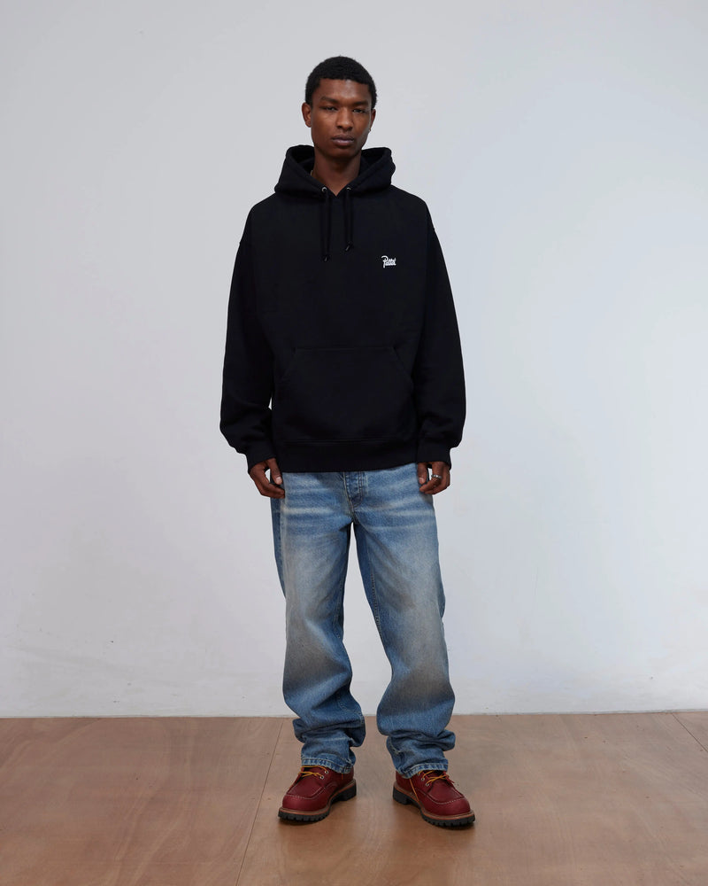 Front view of a model wearing the black Patta Kids Championship Hooded Sweater with blue jeans.