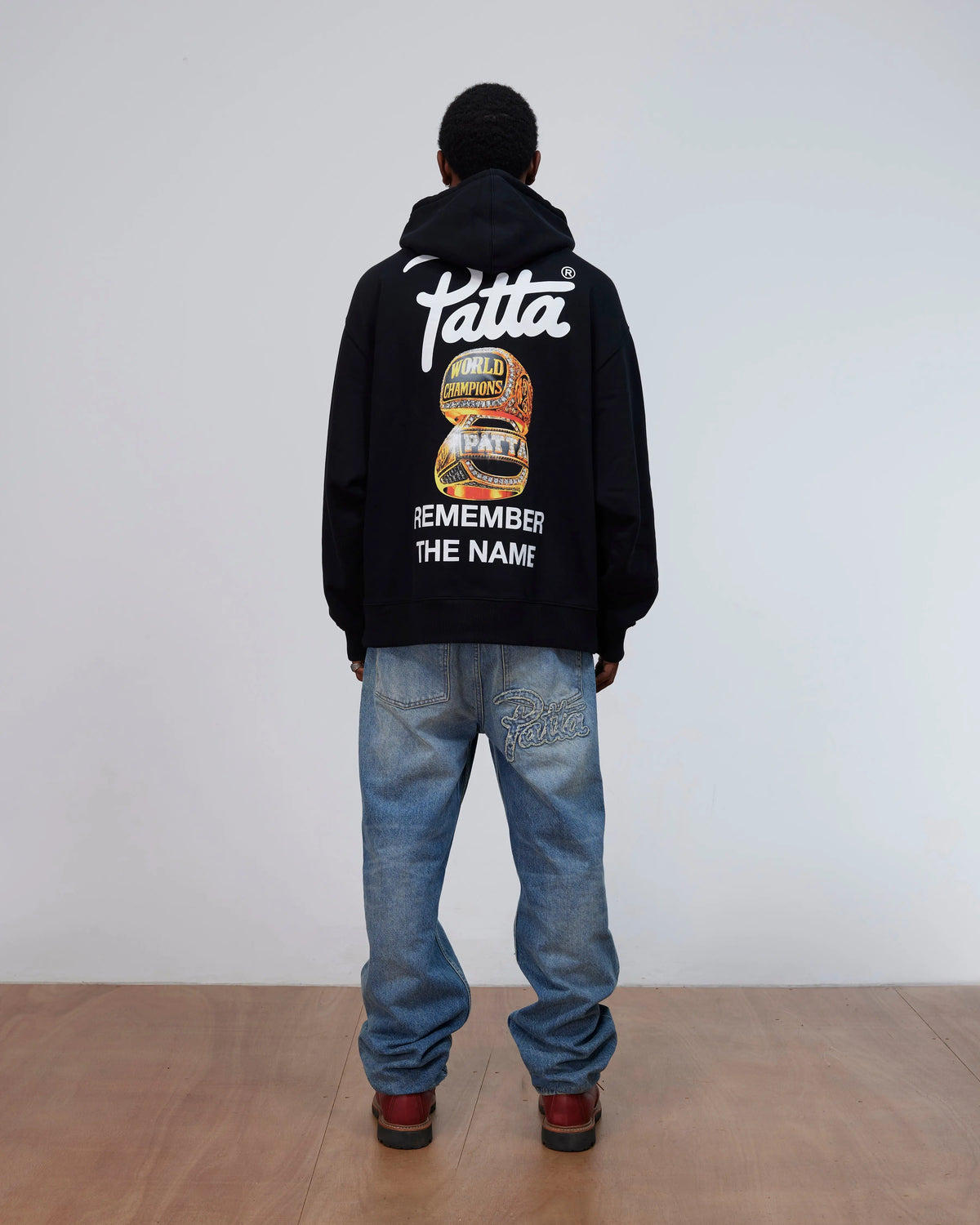 Back view of a model wearing the black Patta Championship Hooded Sweater with back graphic print.