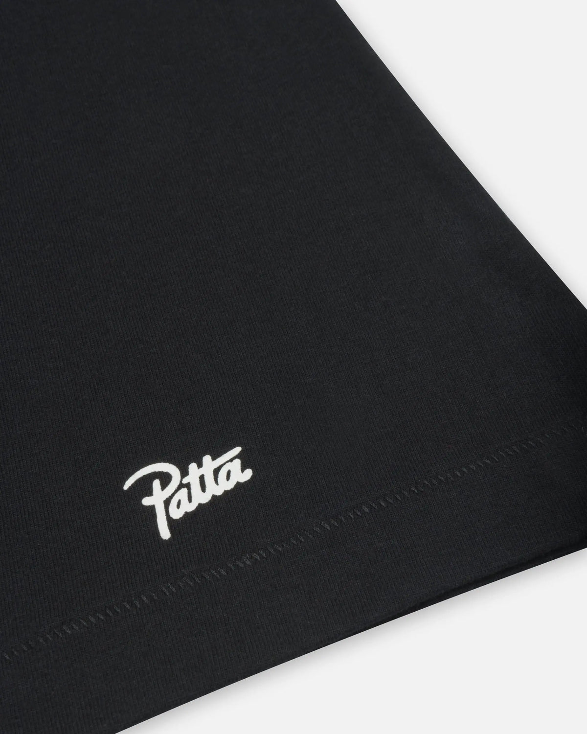 Close-up of the white Patta Script logo printed above the bottom hem on a black cotton t-shirt.