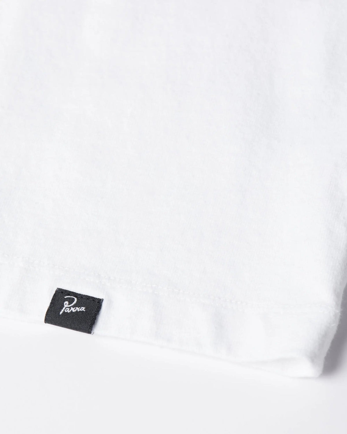 Close-up of the black woven logo label on the hem of the white ByParra Look At It T-shirt.