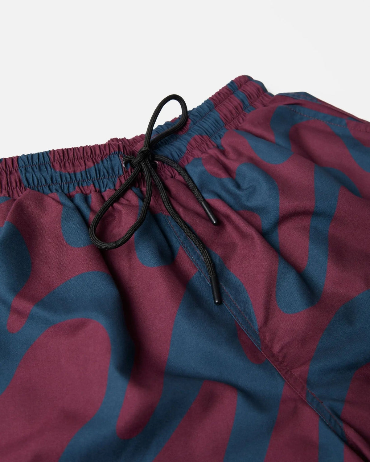Close-up of ByParra Splashed Swim Shorts in burgundy and blue, highlighting the elastic drawstring waistband.