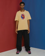 Model wearing the sesame FCB x Patta Culers del Món T-shirt featuring an FC Barcelona heart graphic.