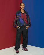 Model wearing the FCB x Patta Culers del Món track jacket against a split red and blue backdrop.