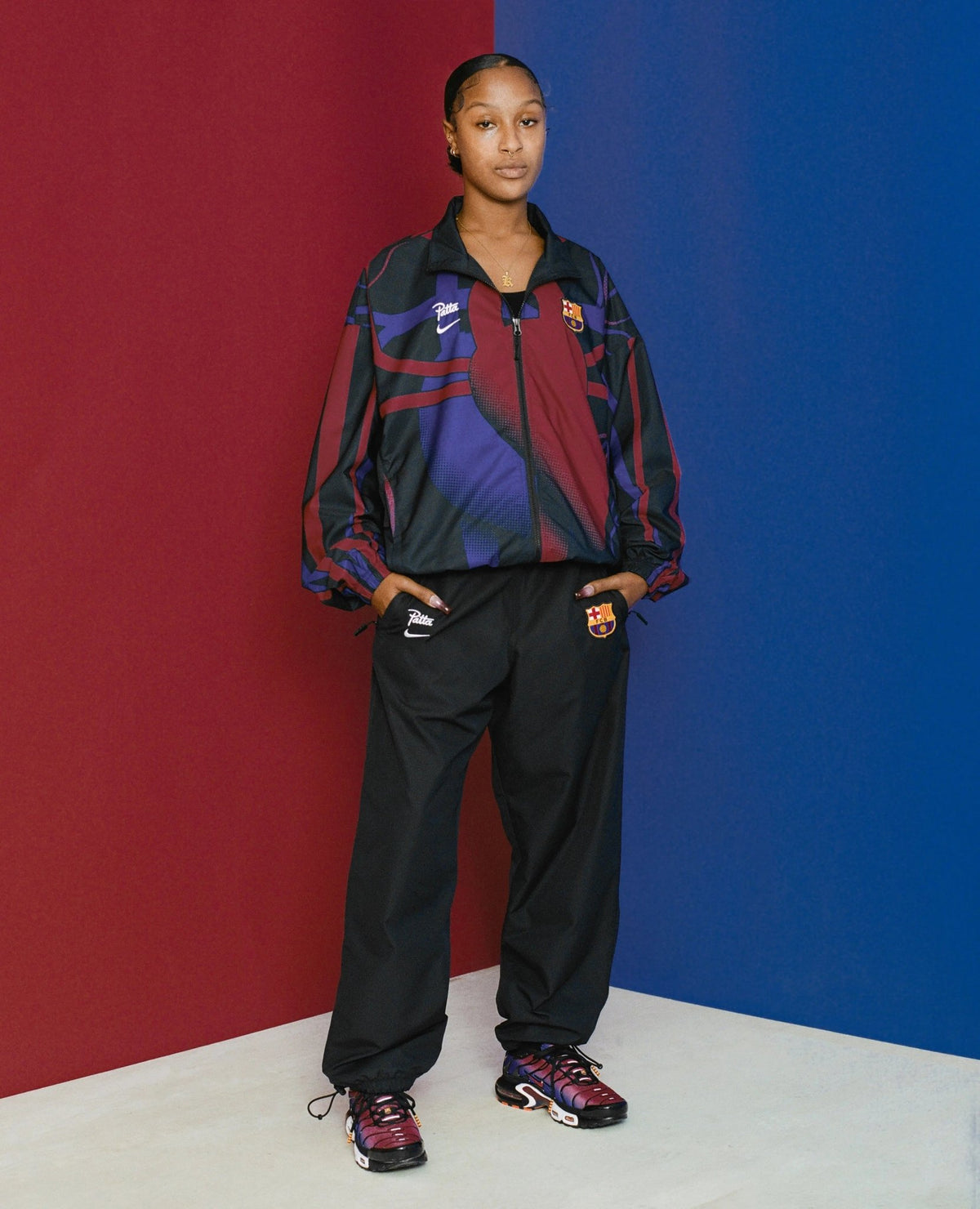 Model wearing the FCB x Patta Culers del Món track jacket against a split red and blue backdrop.
