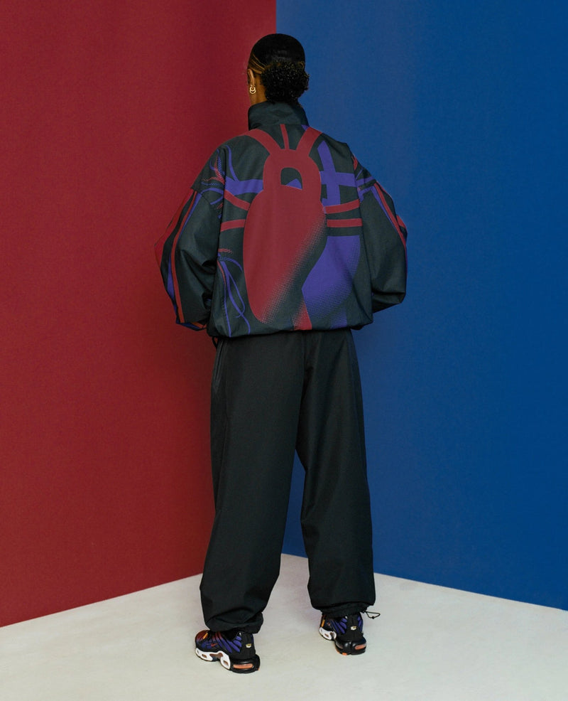 Back view of model wearing the FCB x Patta Culers del Món Track Jacket featuring red and blue graphics.