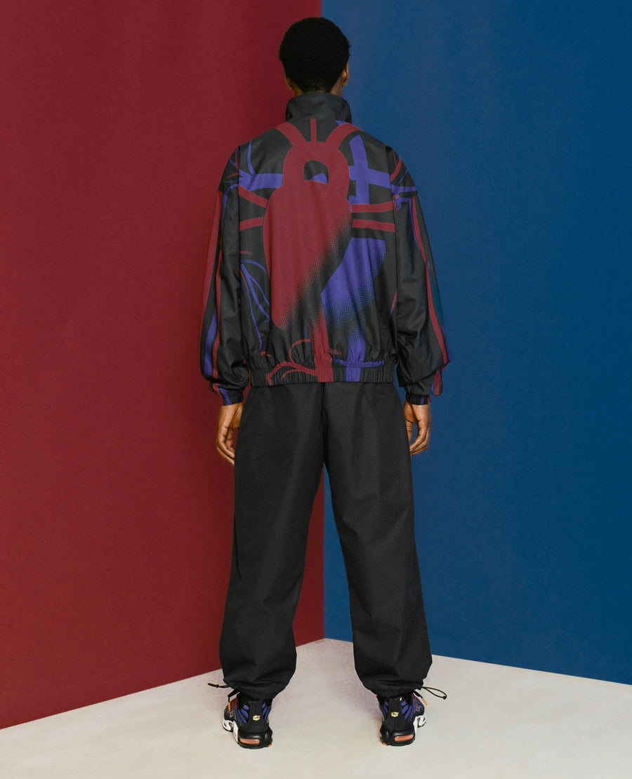 Rear view of a model wearing the FCB x Patta Culers del Món track jacket with red and blue back graphic.