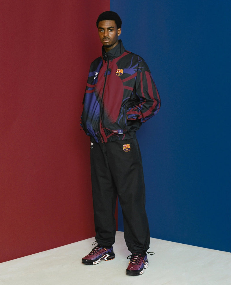 Model wearing the FCB x Patta Culers del Món track jacket against a split red and blue backdrop.