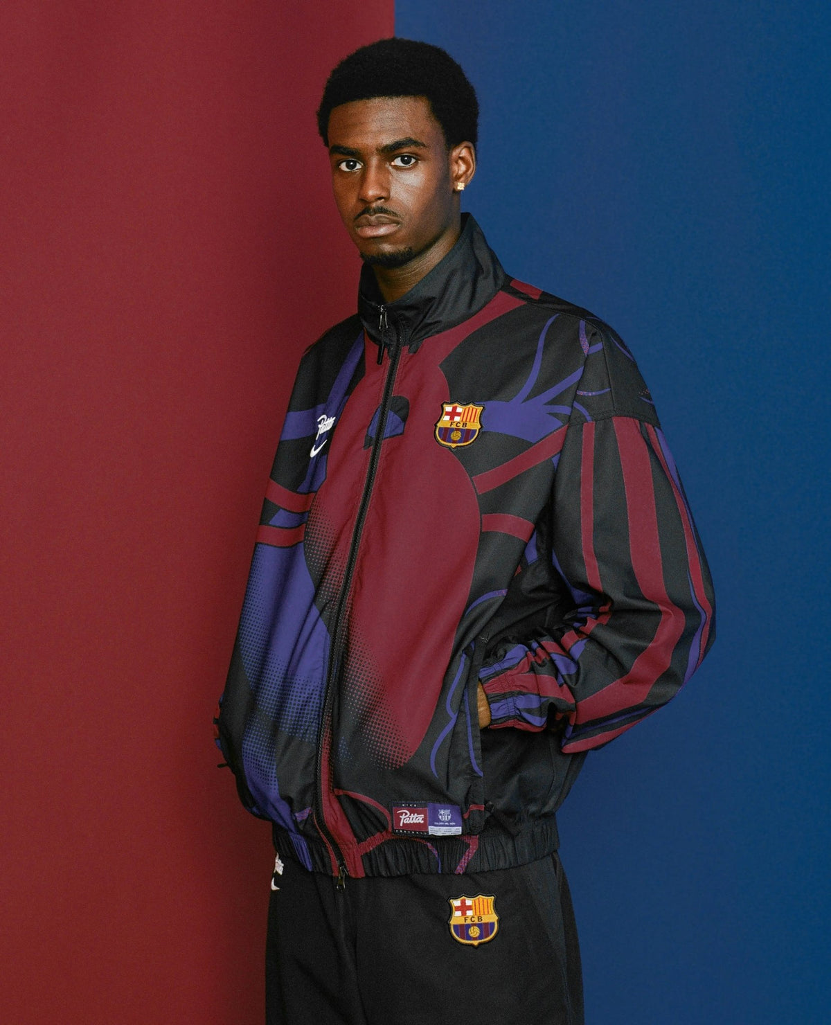 Male model wearing the FCB x Patta Culers del Món Track Jacket against a split red and blue backdrop.