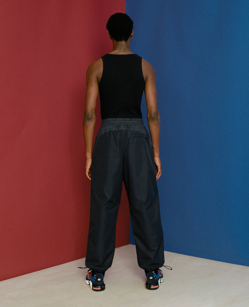 Back view of model wearing black FCB x Patta Culers del Món Track Pants against a red and blue background.