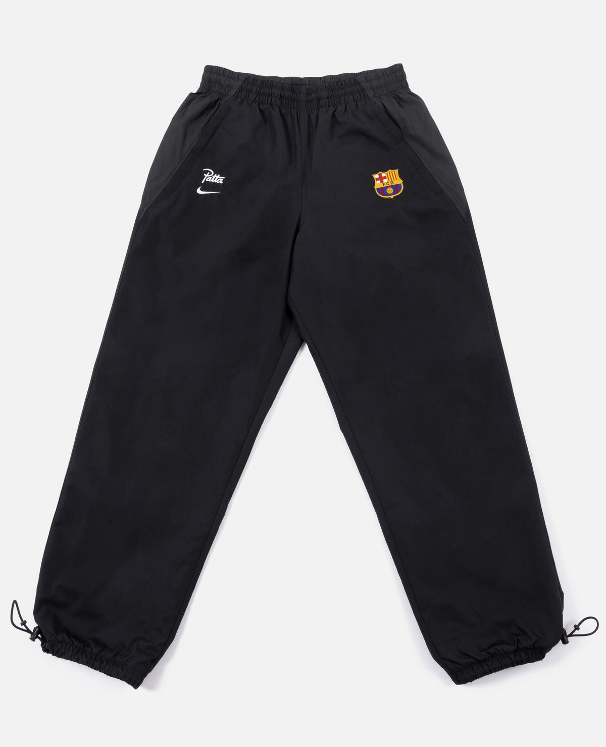 Black FCB x Patta Culers del Món track pants laid flat with FC Barcelona crest and Nike swoosh.