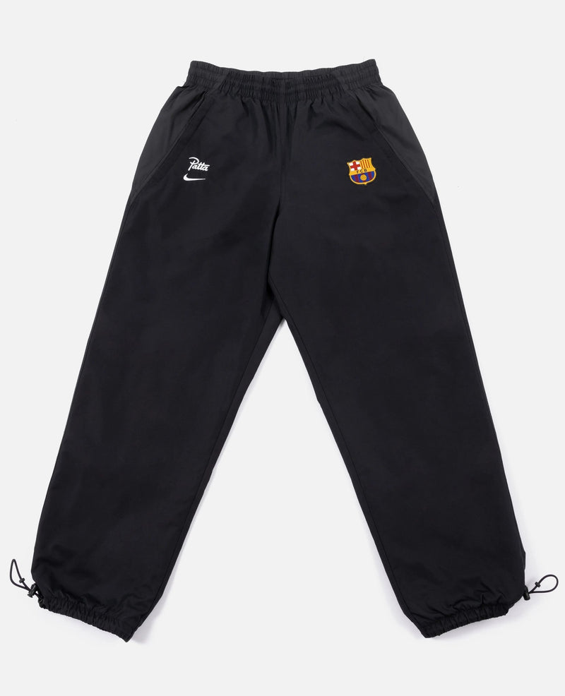 Black FCB x Patta Culers del Món track pants laid flat with FC Barcelona crest and Nike swoosh.