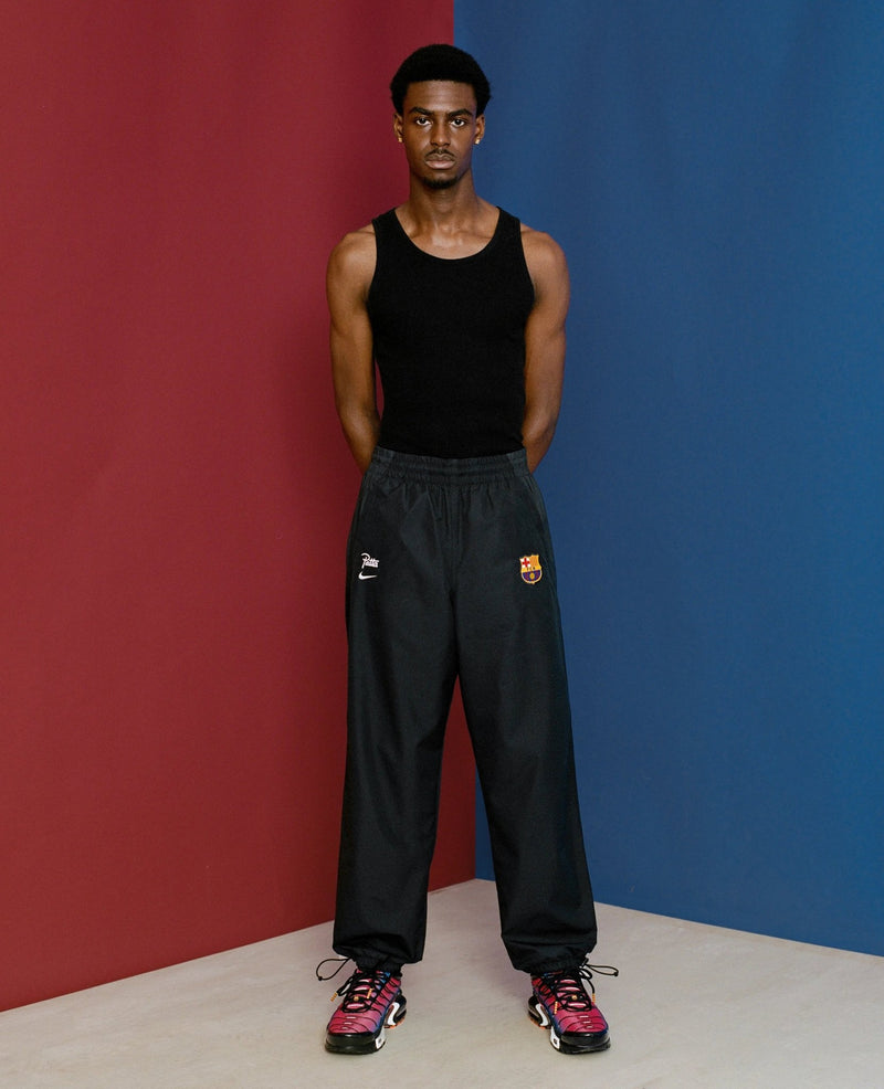 Male model wearing black FCB x Patta Culers del Món track pants against a split red and blue backdrop.