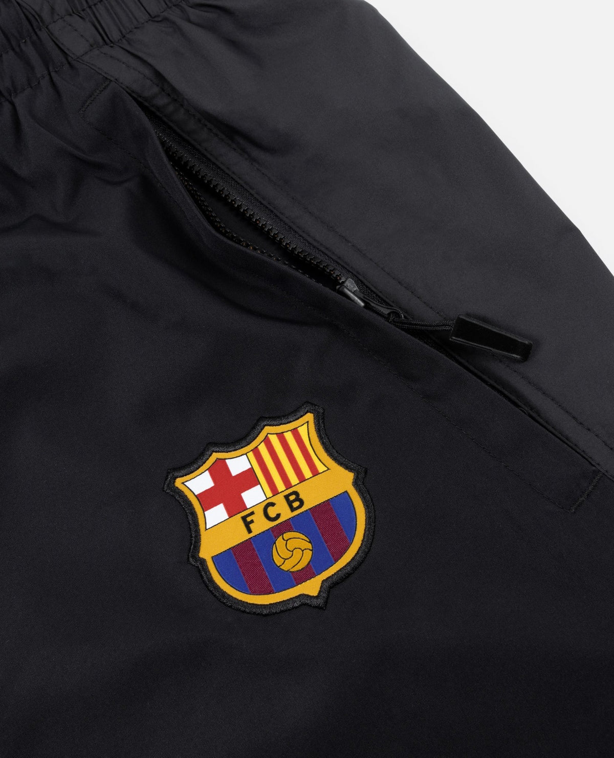 Close-up of FC Barcelona crest badge and zippered pocket on black FCB x Patta track pants.