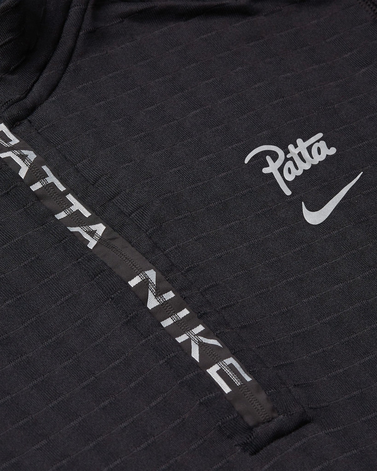 Close-up of the black Nike x Patta Running Team half-zip longsleeve with branded zipper tape and chest logo.