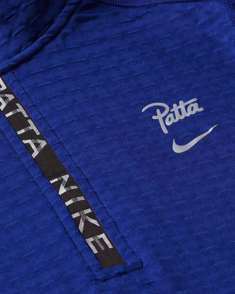 Close-up of the deep royal blue Nike x Patta half-zip longsleeve with reflective logo and branded zipper tape.
