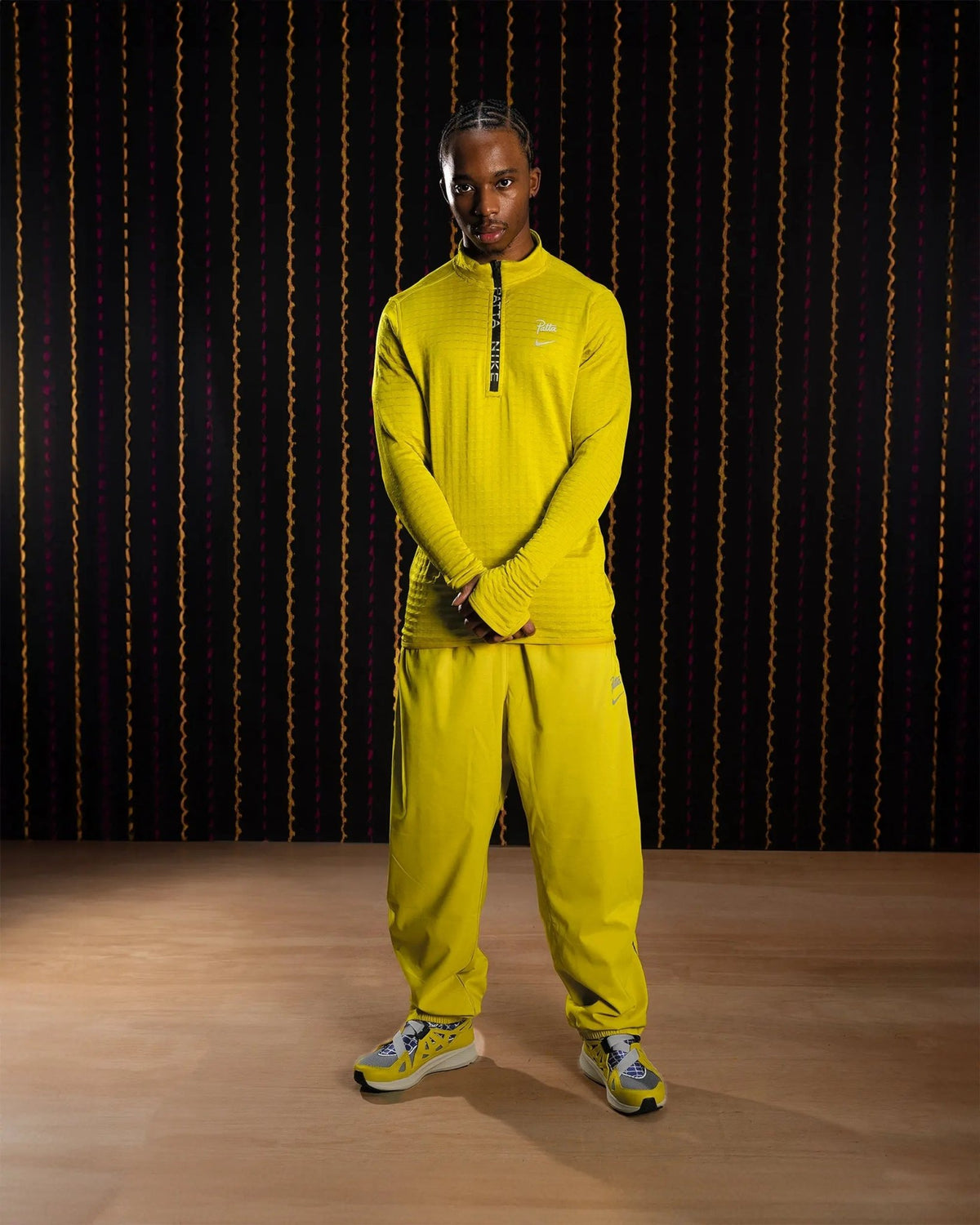 Model wearing the Nike x Patta Running Team half-zip longsleeve in saffron quartz yellow with matching track pants.
