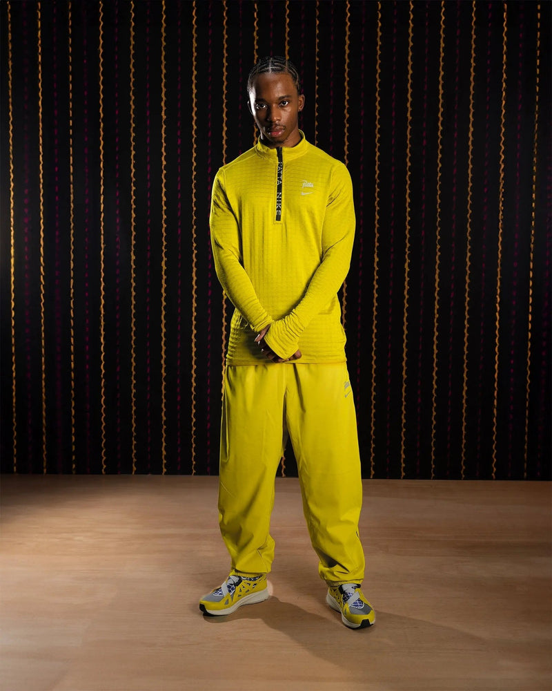 Model wearing the Nike x Patta Running Team half-zip longsleeve in saffron quartz yellow with matching track pants.