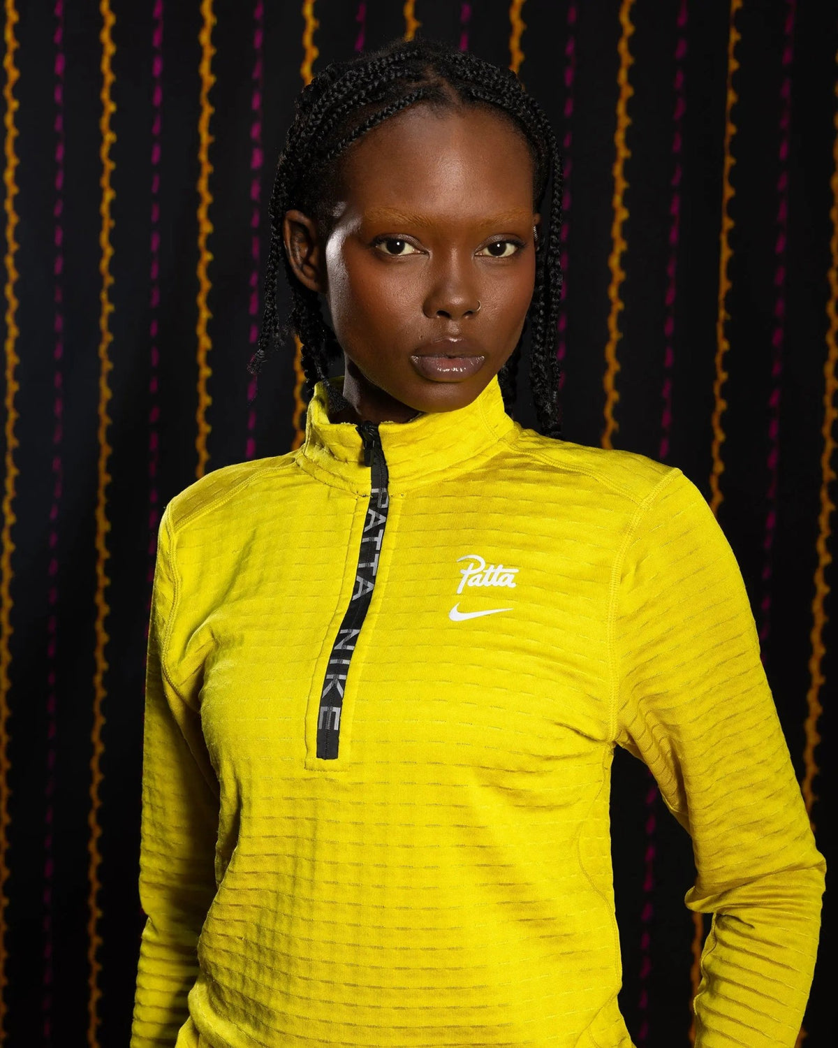Model wearing the Nike x Patta Running Team half-zip longsleeve in saffron quartz yellow against a dark backdrop.