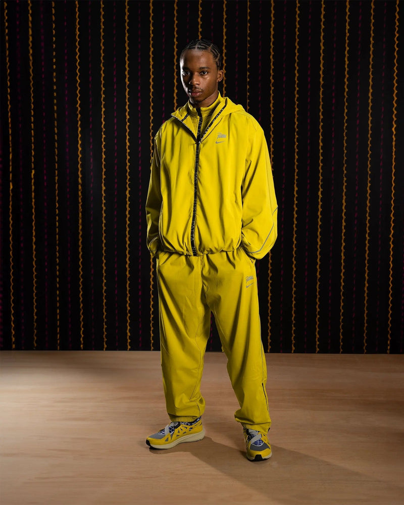 Model wearing the saffron quartz Nike x Patta Running Team hooded track jacket and matching track pants.